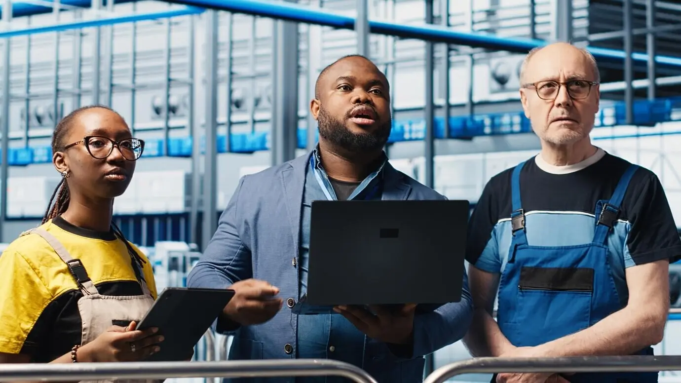 Менеджер умной фабрики обучает рабочих управлению роботизированными манипуляторами с помощью ноутбука.
